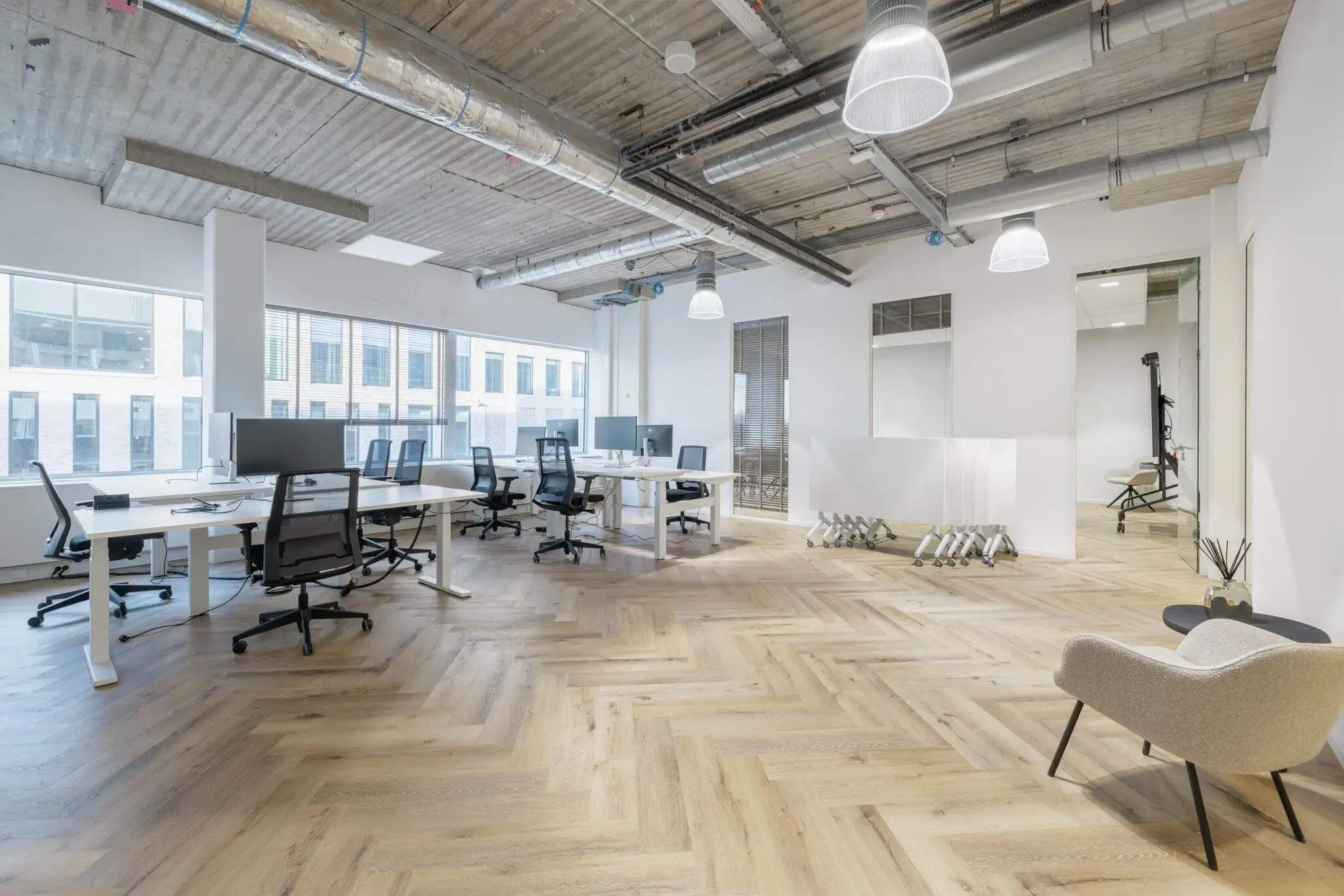 Een moderne en lichte kantoorruimte met meerdere bureaus en stoelen.