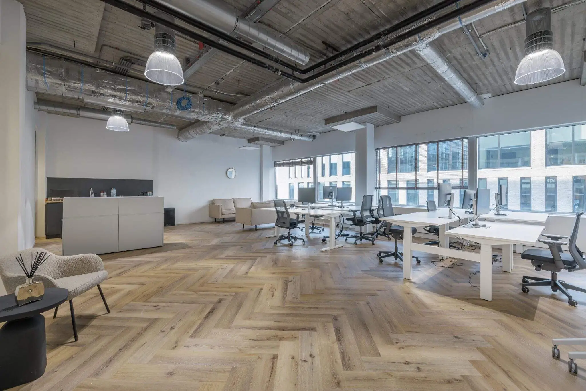 Een ruime, moderne kantoorruimte met houten vloer, bureaus, stoelen en een zithoek.