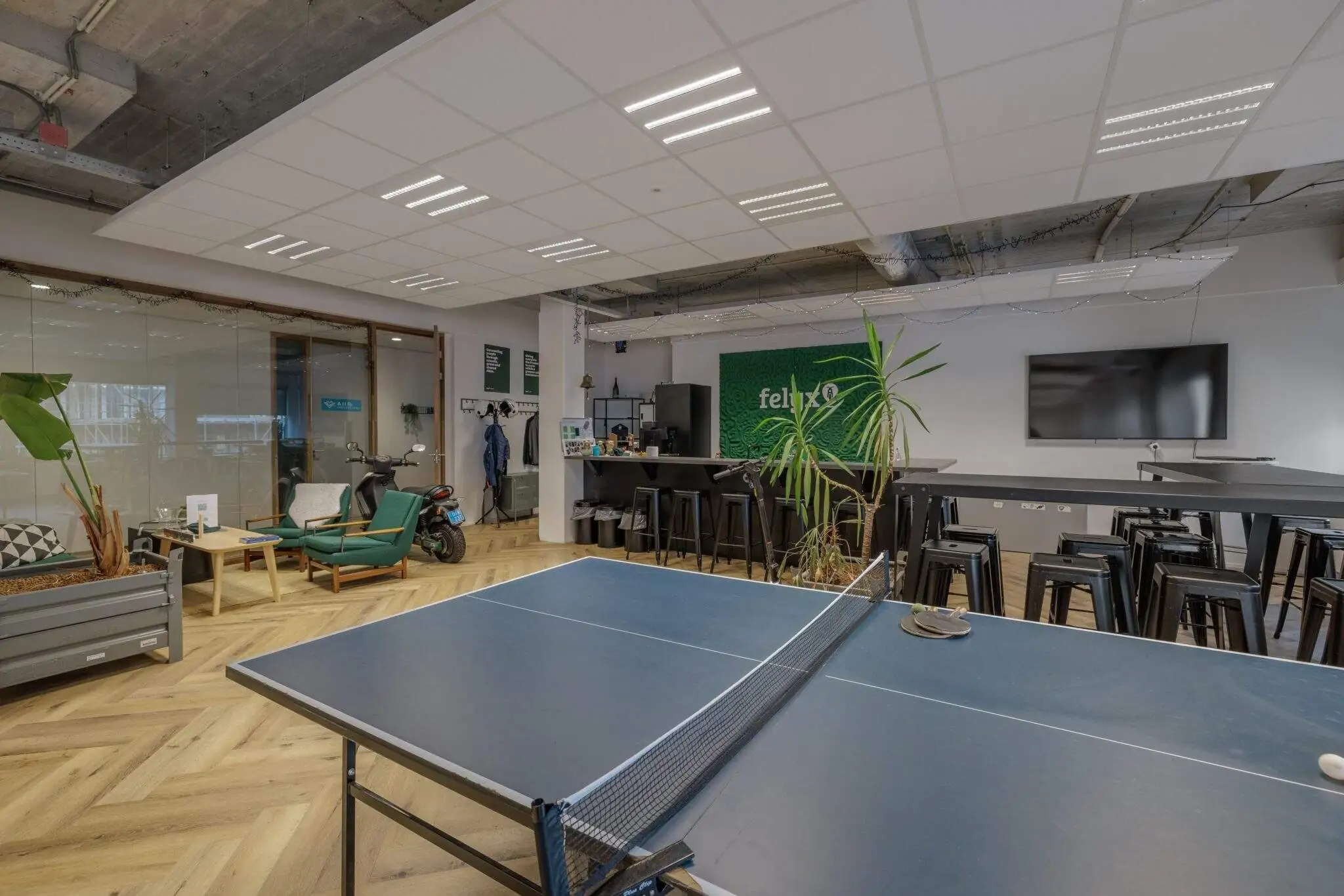 Kantoorruimte met een tafeltennistafel, zithoek, scooter, en een bar met krukken.