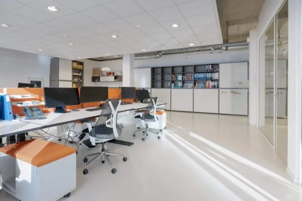 Een moderne en lichte kantoorruimte met bureaus, schermen en boekenplanken.