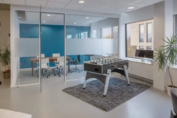 Een moderne kantoorruimte met een glazen vergaderruimte en een tafelvoetbaltafel.