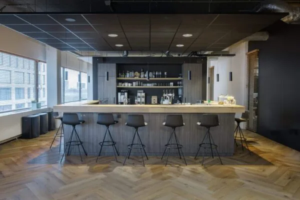 Moderne kantoorbar met houten vloer en hoge zwarte stoelen langs een toonbank.