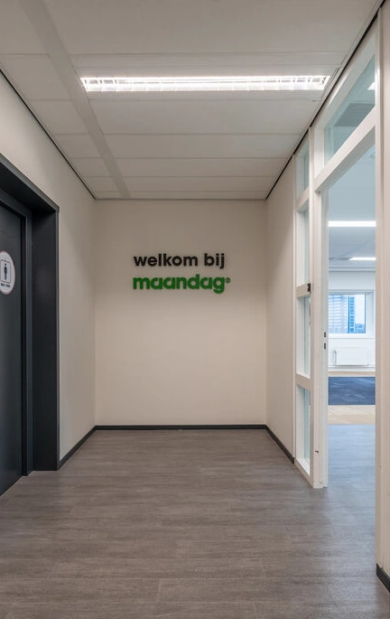 Ingang van een kantoorruimte met de tekst "welkom bij maandag" op de muur.