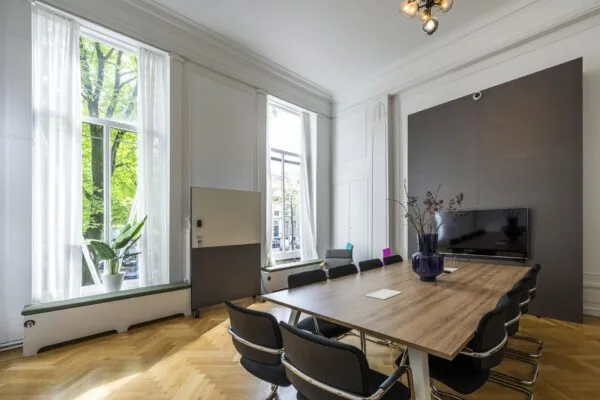 Vergaderruimte aan de Herengracht met een lange houten tafel, moderne stoelen, grote ramen en een flatscreen.