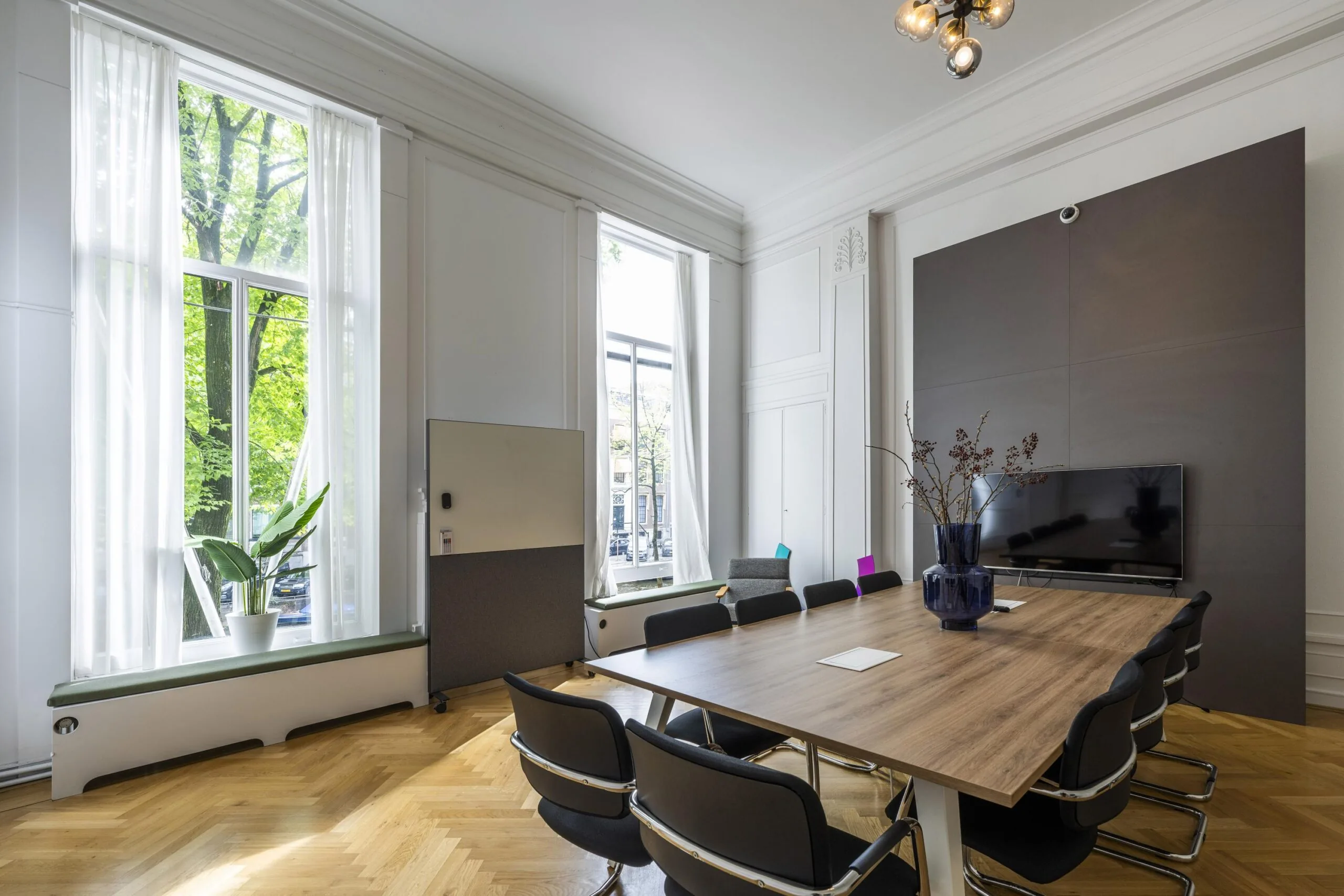 Vergaderruimte aan de Herengracht met een lange houten tafel, moderne stoelen, grote ramen en een flatscreen.