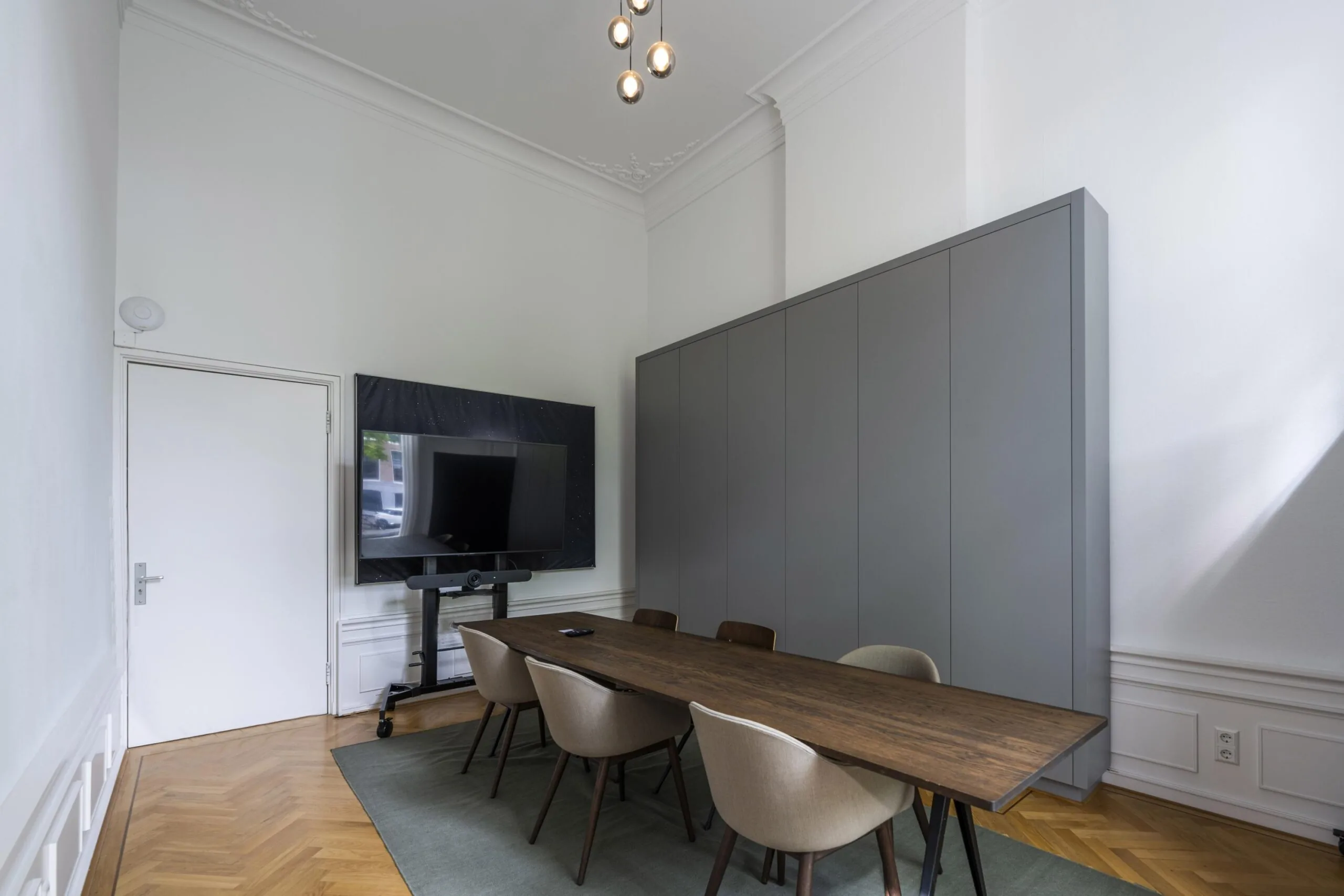 Vergaderruimte aan de Herengracht met een lange houten tafel, zes stoelen, een flatscreen-tv en hoge grijze kasten.