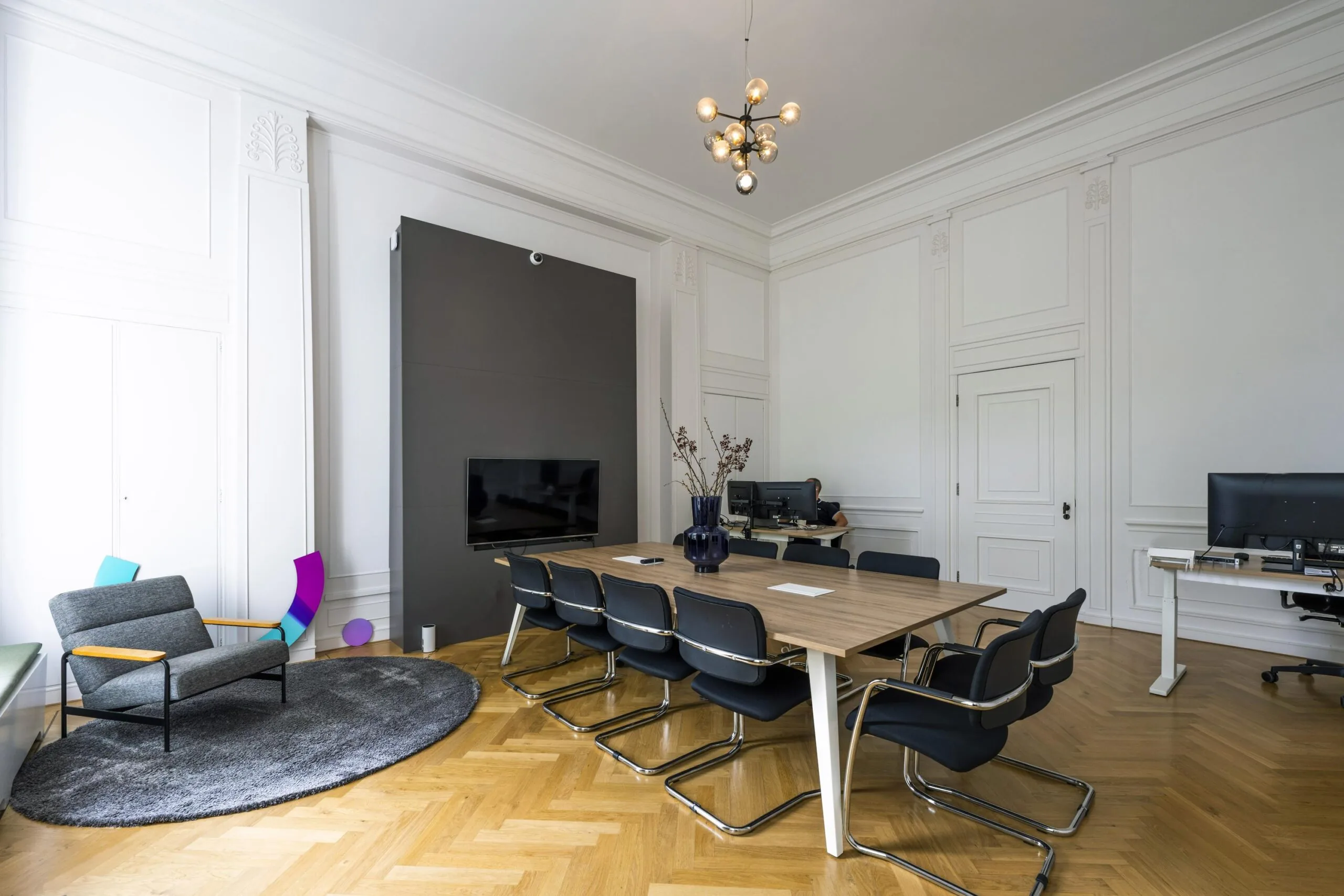 Moderne vergaderruimte aan de Herengracht met houten vloer, grote tafel, designstoelen, flatscreen en sierlijke witte wandpanelen.