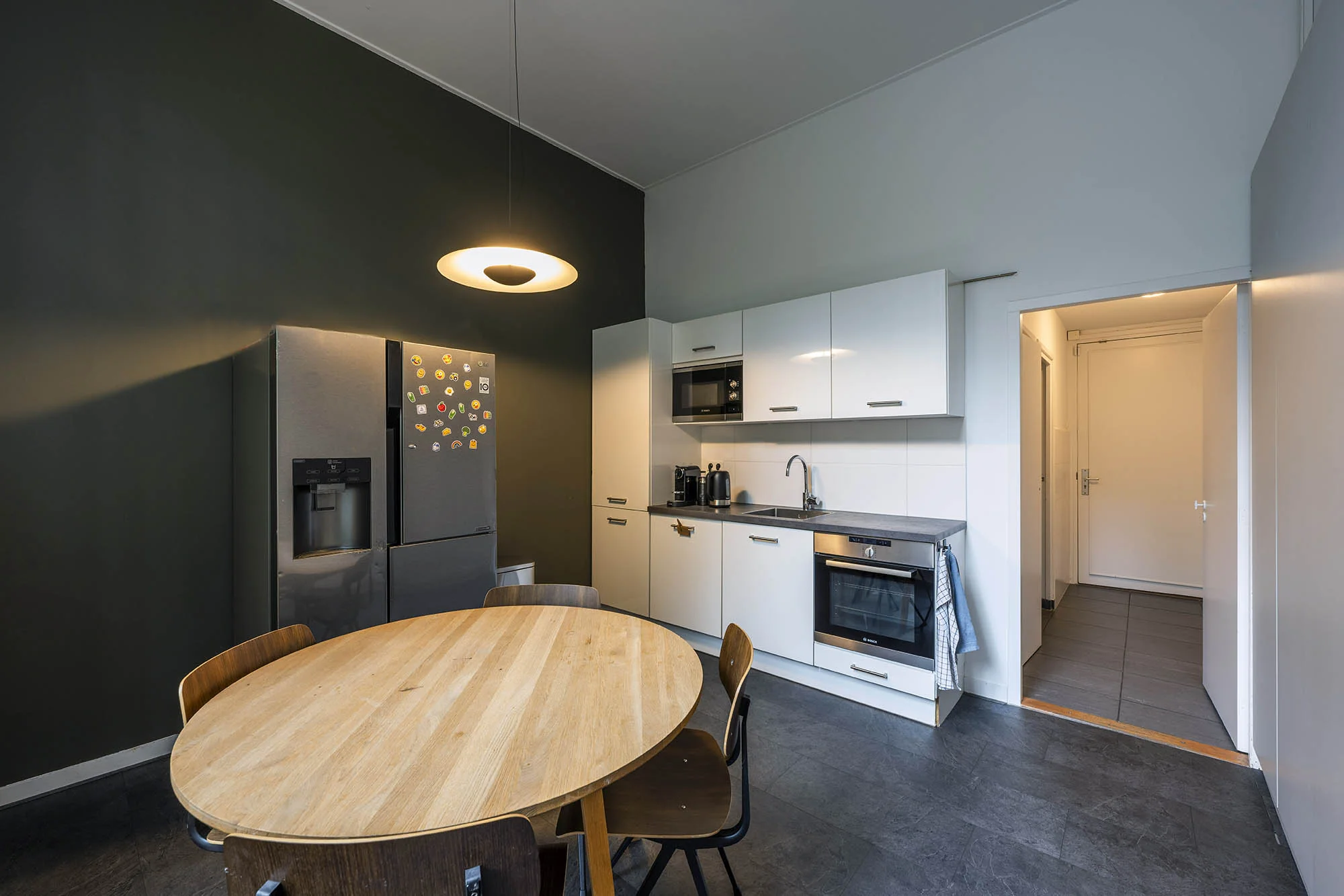 Moderne keuken aan de Herengracht met witte kasten, een ronde houten eettafel en een donkere koelkast met magneten.