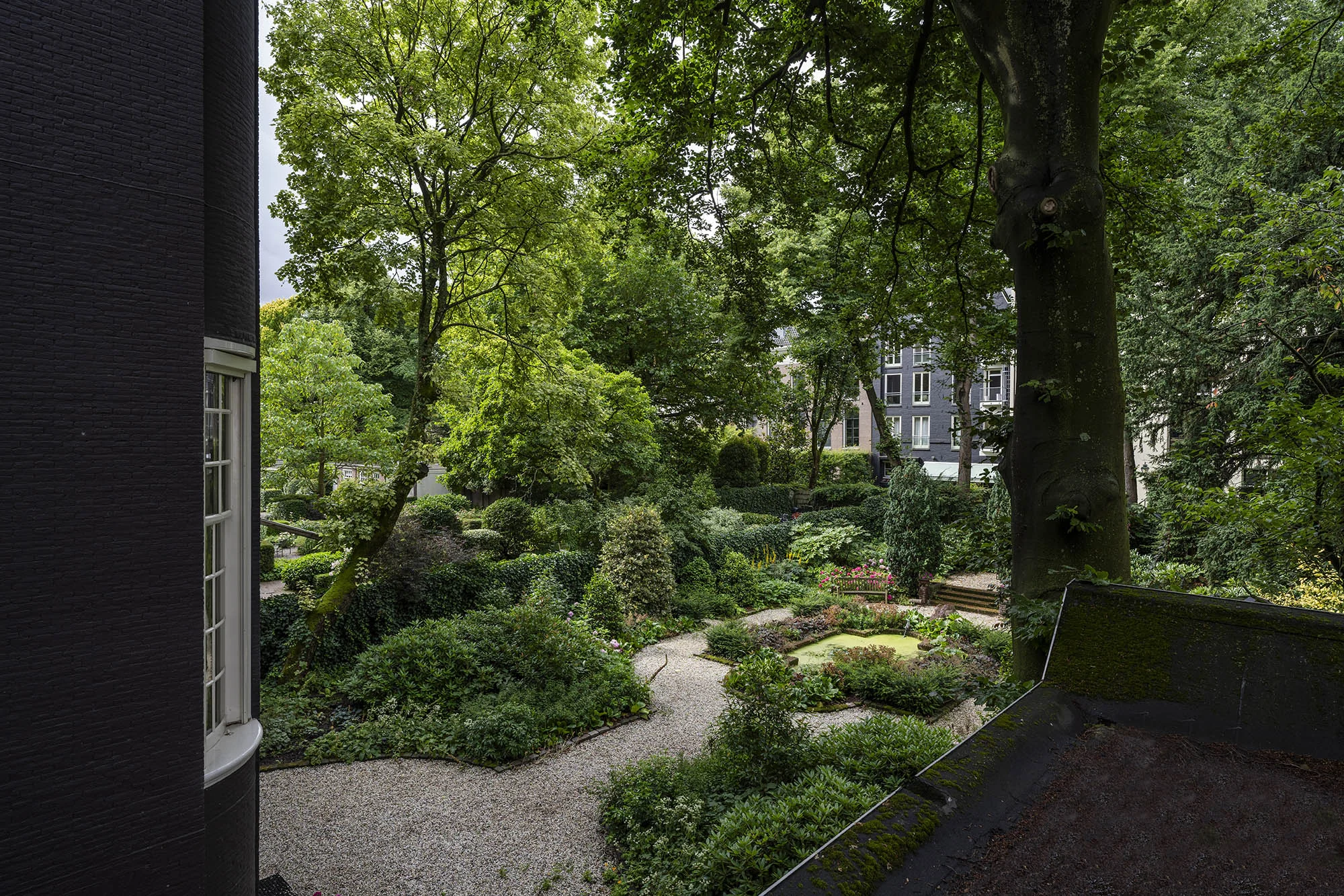Luxe stadstuin aan de Herengracht met kronkelende grindpaden, vijver en weelderig groen omringd door historische panden.