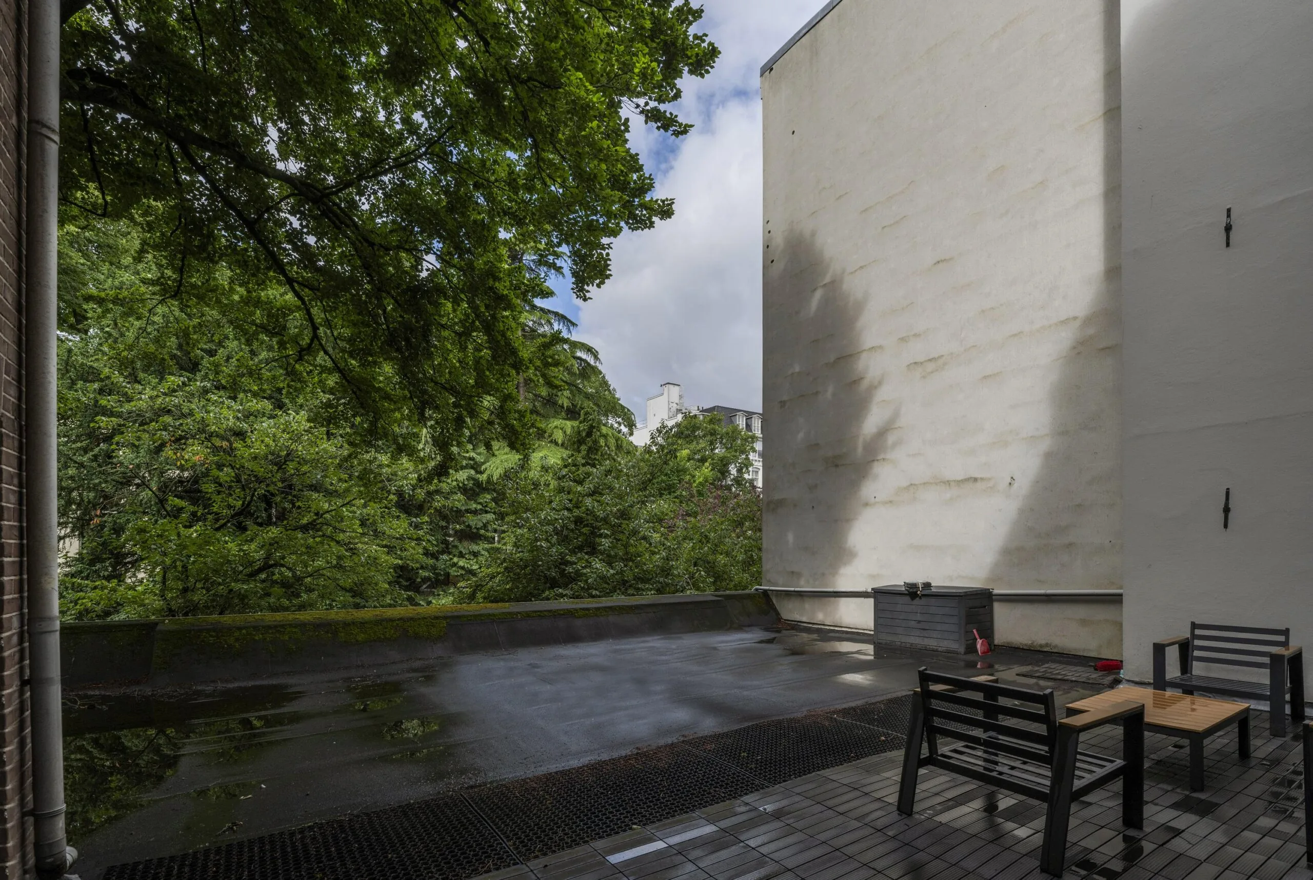 Terras met zwarte tuinmeubelen en uitzicht op groene bomen aan de achterzijde van een pand aan de Herengracht.