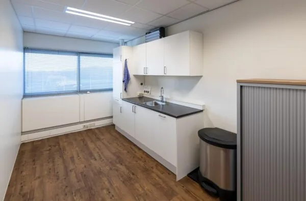 Kleine, moderne pantry met witte keukenkasten, donker aanrechtblad en houten vloer in een kantoor aan de Seattleweg.