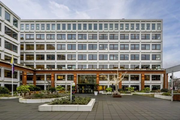 Vooraanzicht van een modern kantoorgebouw aan de Stroombaan met een betegeld plein en beplanting.