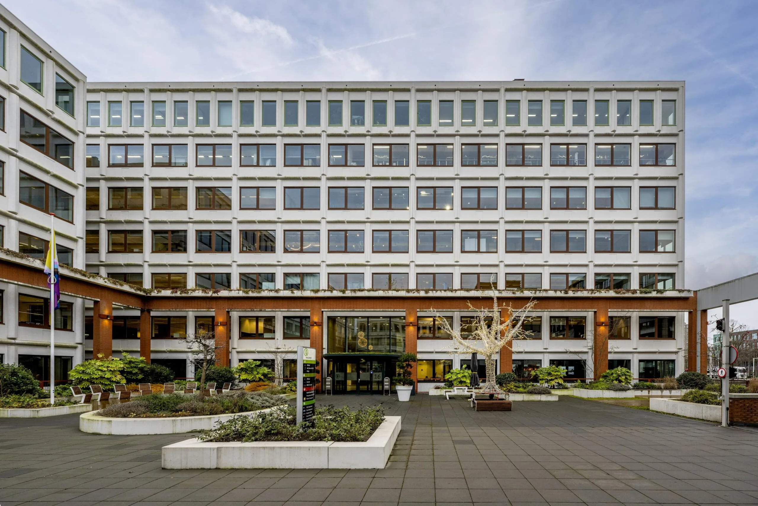 Vooraanzicht van een modern kantoorgebouw aan de Stroombaan met een betegeld plein en beplanting.