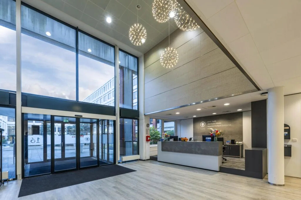 Moderne, lichte entreehal van een kantoorpand aan de Stroombaan met glazen schuifdeuren en een receptiebalie.
