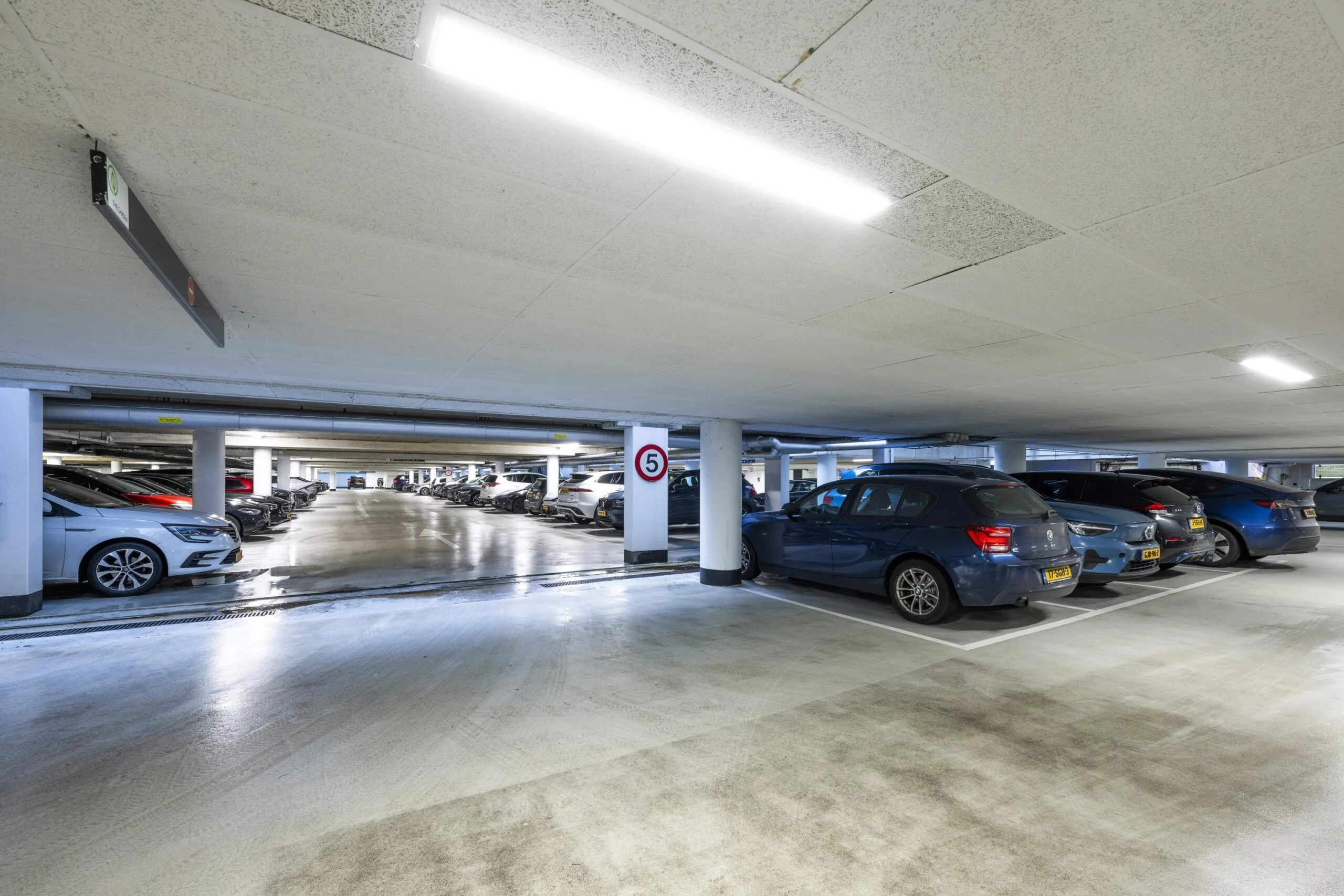 Ondergrondse parkeergarage met geparkeerde auto's en een snelheidsbeperking van 5 km/u.
