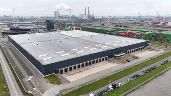 Luchtfoto van een groot distributiecentrum aan de Koerilenstraat in een havengebied met zeecontainers en industriële gebouwen op de achtergrond.