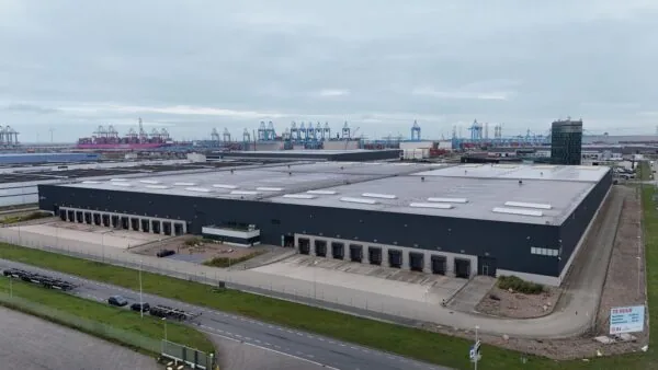 Luchtfoto van een groot distributiecentrum aan de Koerilenstraat in een havengebied met containerkranen op de achtergrond.