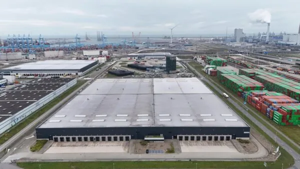 Luchtfoto van een groot magazijn aan de Koerilenstraat in het Rotterdamse havengebied, omringd door containers en industriële gebouwen.