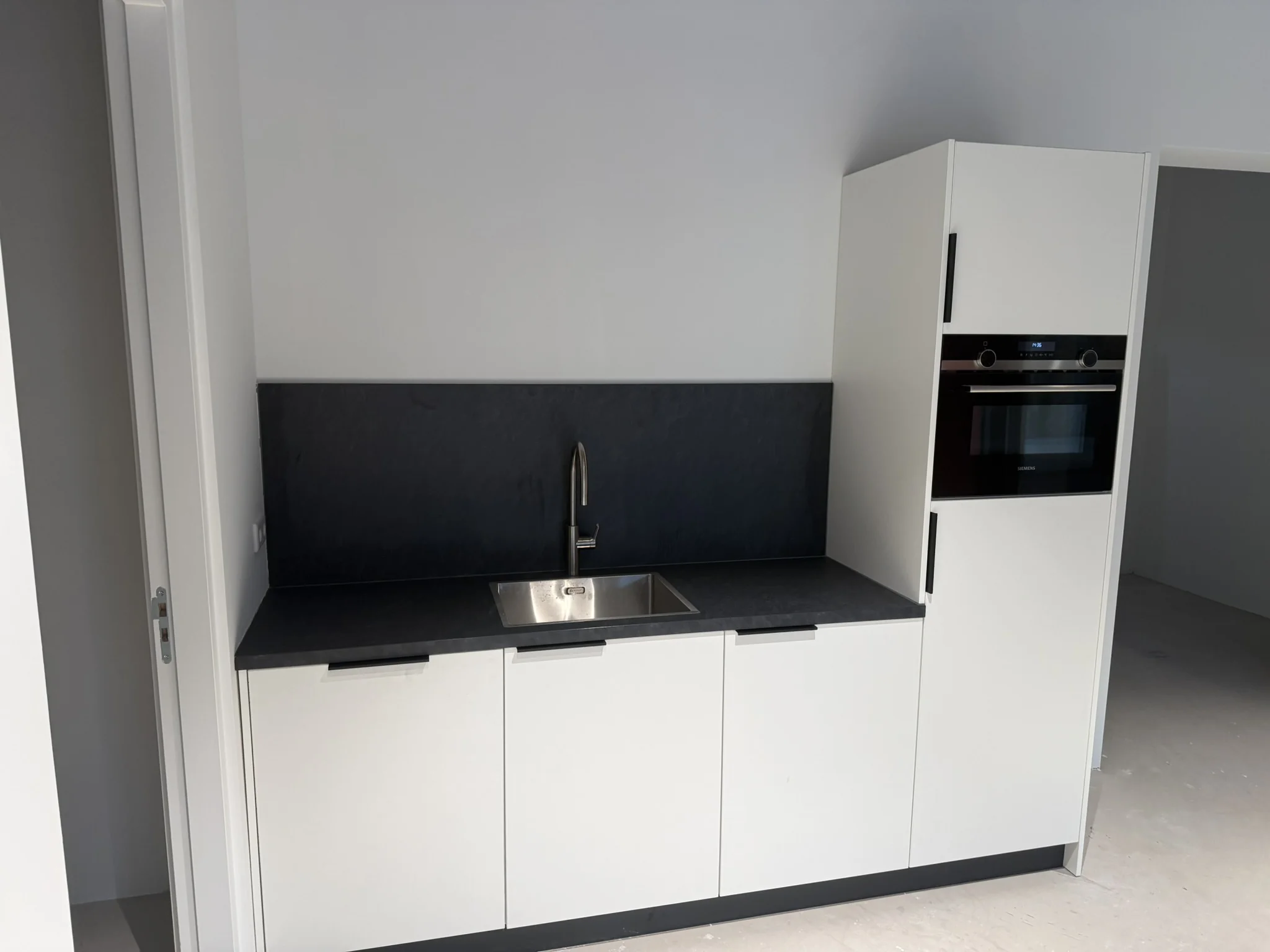 Moderne witte keuken met zwarte werkblad, ingebouwde oven en spoelbak aan de Saturnusstraat.