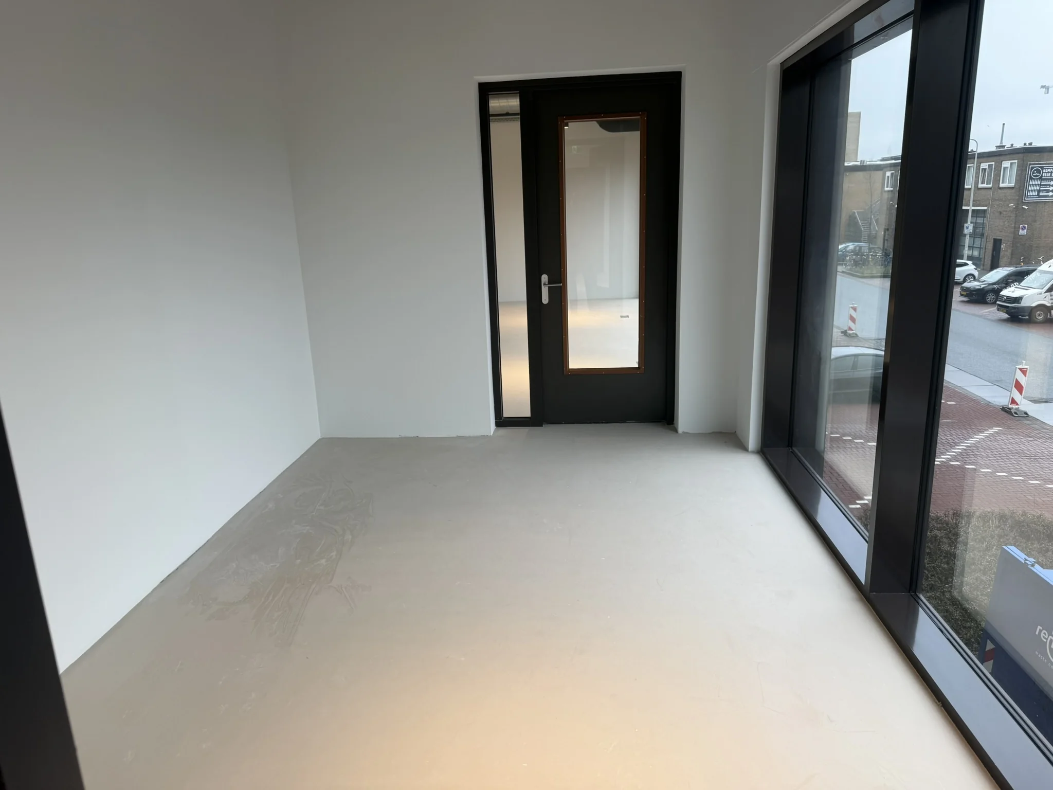 Lege kamer met grijze vloer, witte muren, zwarte deur en grote ramen aan de straatkant op de Saturnusstraat.