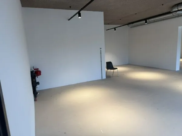 Lege, industriële ruimte aan de Saturnusstraat met witte muren, betonvloer en een enkele zwarte stoel.