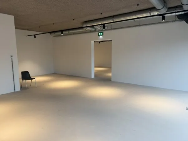 Lege, industrieel ogende ruimte aan de Saturnusstraat met een enkele zwarte stoel en zichtbare ventilatiebuizen aan het plafond.