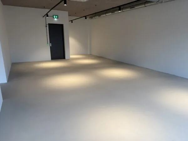 Leeg industrieel ogend interieur aan de Saturnusstraat met grijze vloer, witte muren en spotverlichting.