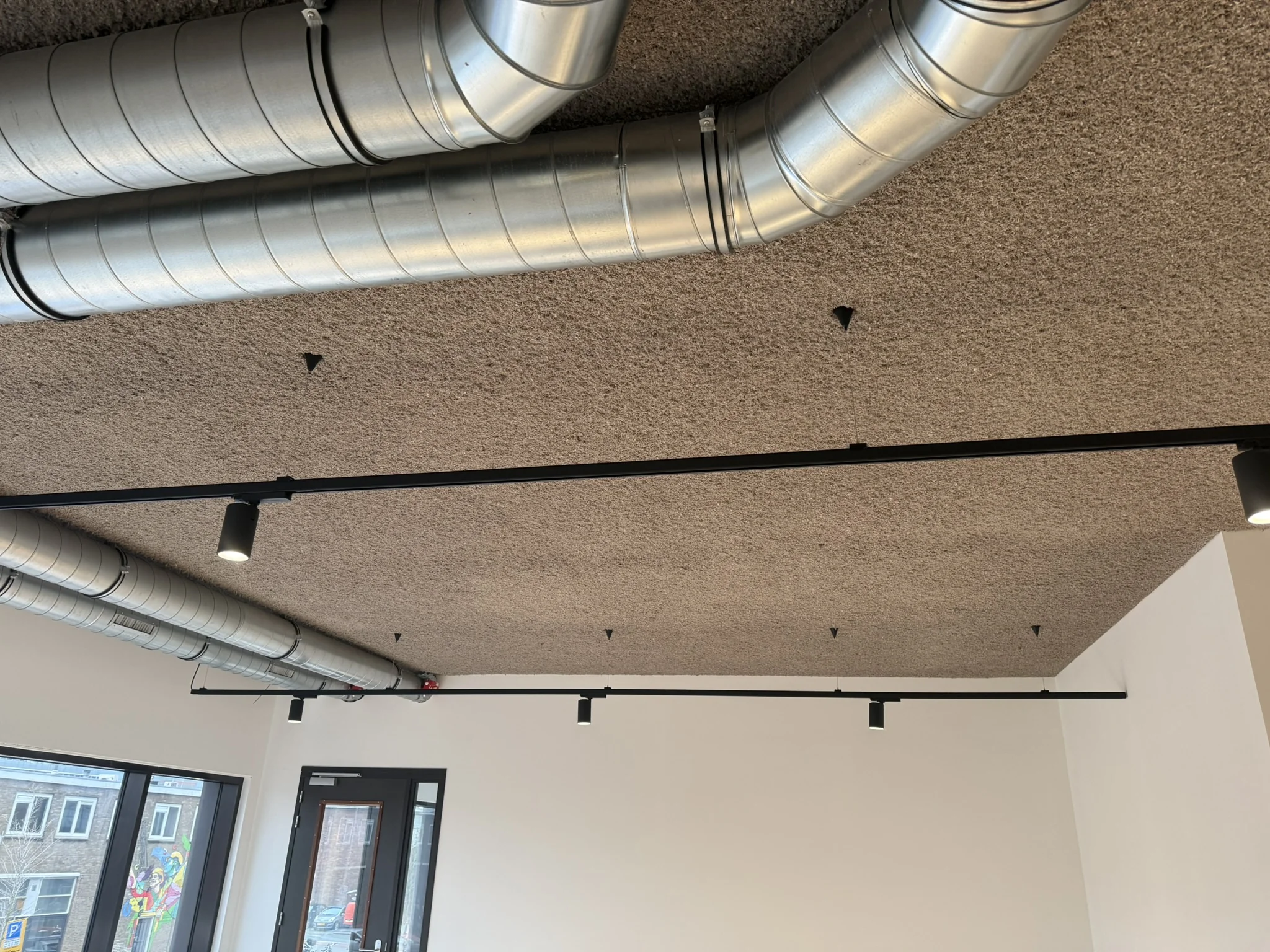 Plafond van een modern kantoor aan de Saturnusstraat met zichtbare ventilatiebuizen en zwarte railverlichting.