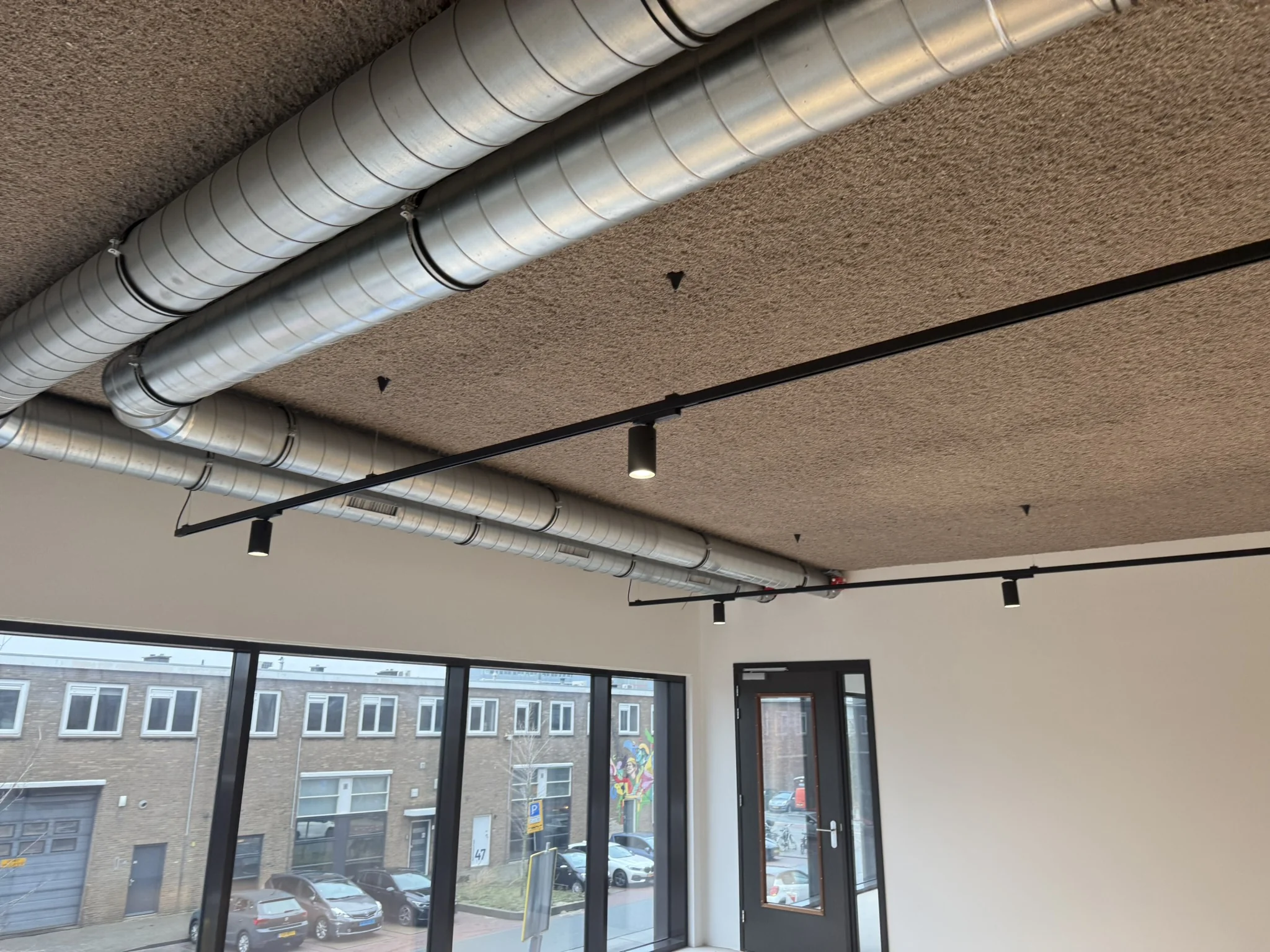 Plafond van een modern kantoor aan de Saturnusstraat met zichtbare ventilatiebuizen en zwarte spots.