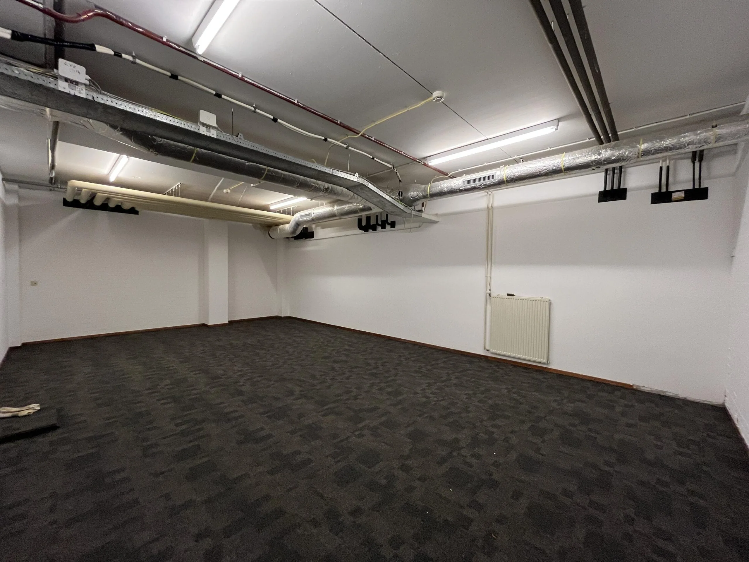Leeg kantoorpand aan de Euclideslaan met zicht op systeemplafond, leidingen en donker tapijt.