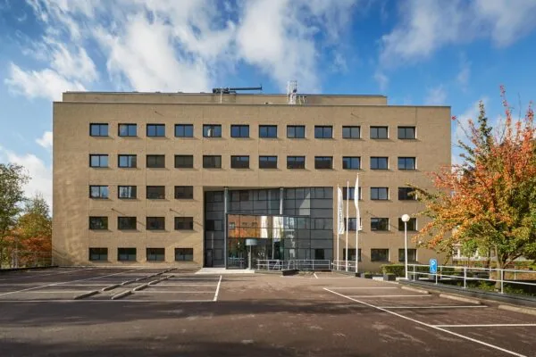 Kantoorgebouw aan de Euclideslaan met glazen entree, vlaggenmasten en lege parkeerplaatsen op de voorgrond.