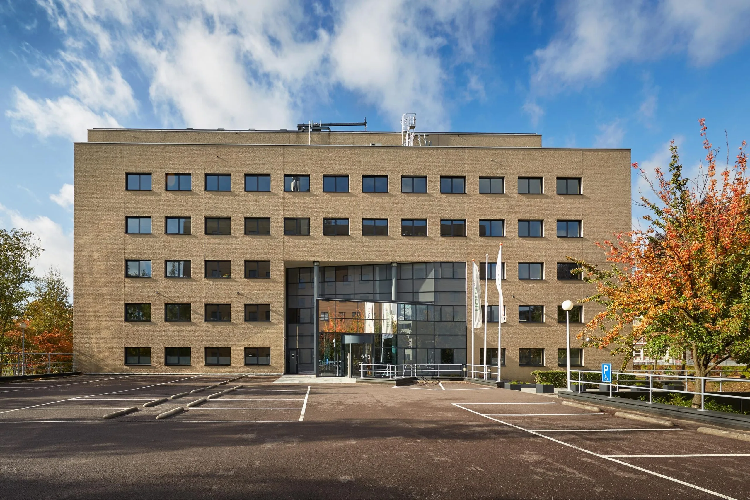 Kantoorgebouw aan de Euclideslaan met glazen entree, vlaggenmasten en lege parkeerplaatsen op de voorgrond.