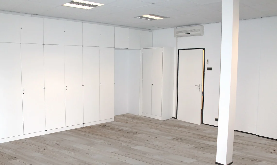 Lege kamer met witte kastenwand, deur en airconditioning aan het plafond.