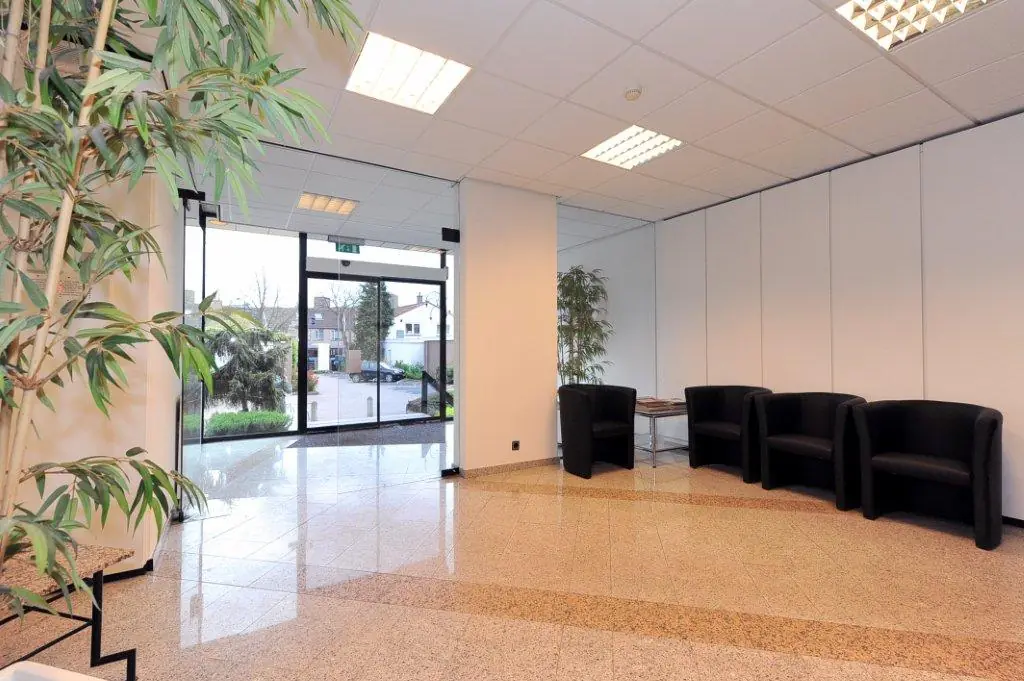Moderne wachtruimte met zwarte stoelen, planten en een glazen entree aan het Oosteinde.