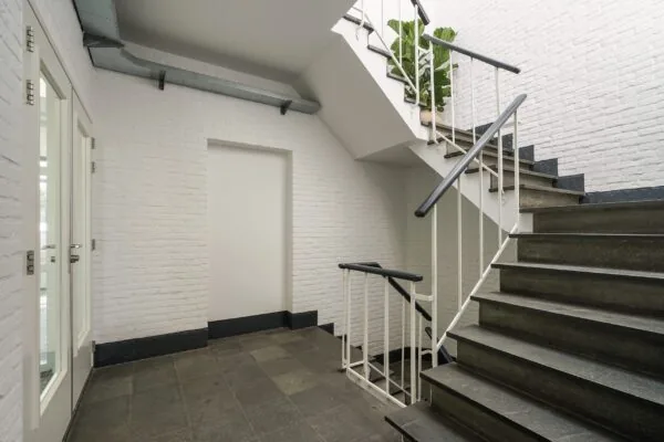 Moderne trappenhal in een gebouw aan de Mercuriusweg met witte bakstenen muren en donkergrijze stenen trap.