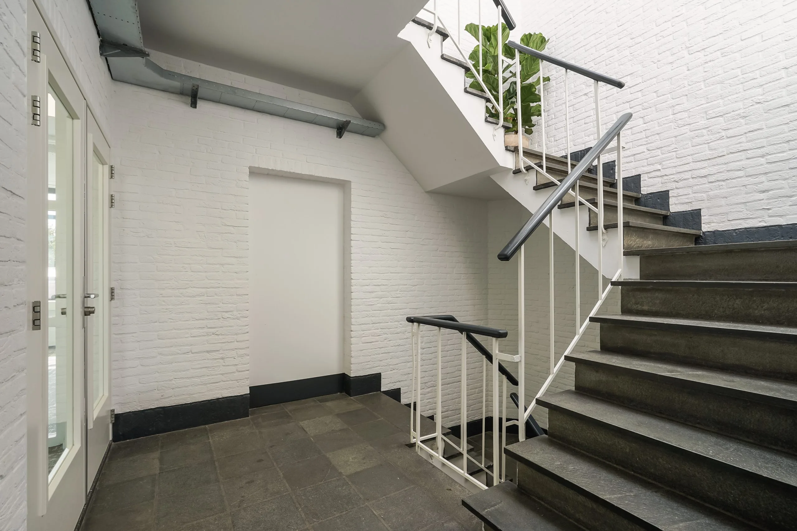 Moderne trappenhal in een gebouw aan de Mercuriusweg met witte bakstenen muren en donkergrijze stenen trap.