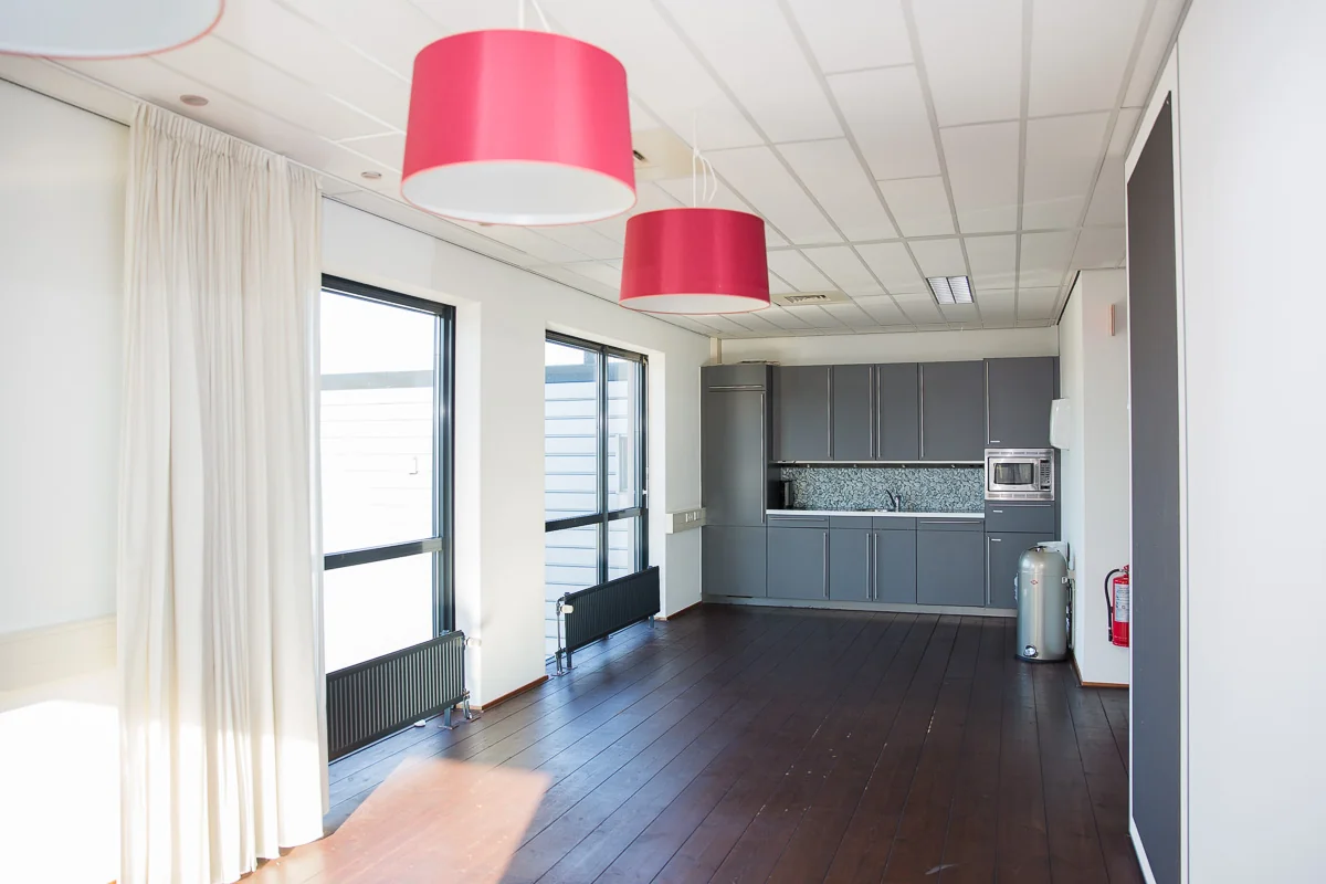 Moderne kantoorkeuken aan de Laan van s-Gravenmade met grijze kasten, houten vloer en roze hanglampen.