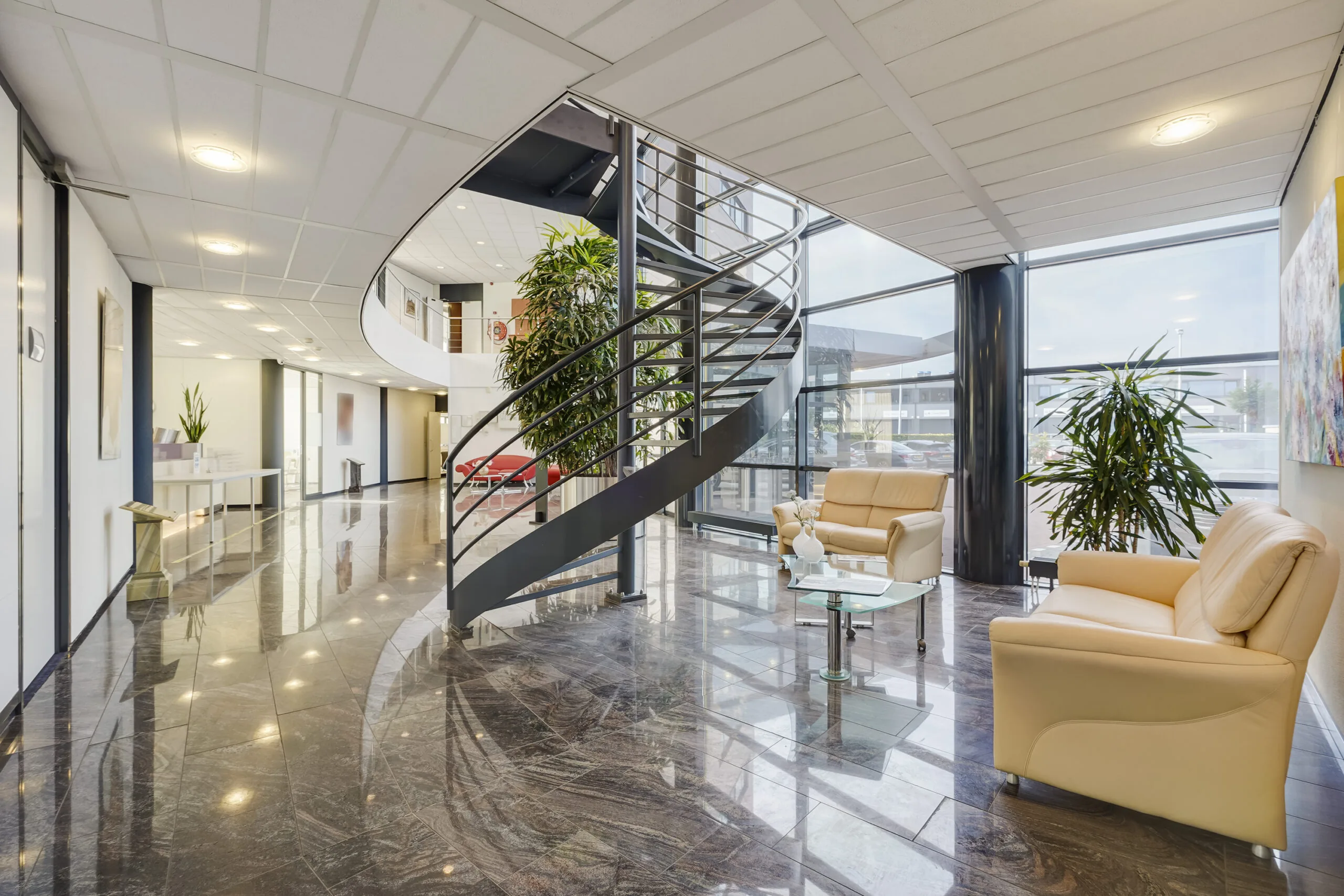 Moderne en lichte kantoorentree aan de Laan van ’s-Gravenmade met glazen gevel, wenteltrap en zithoek.