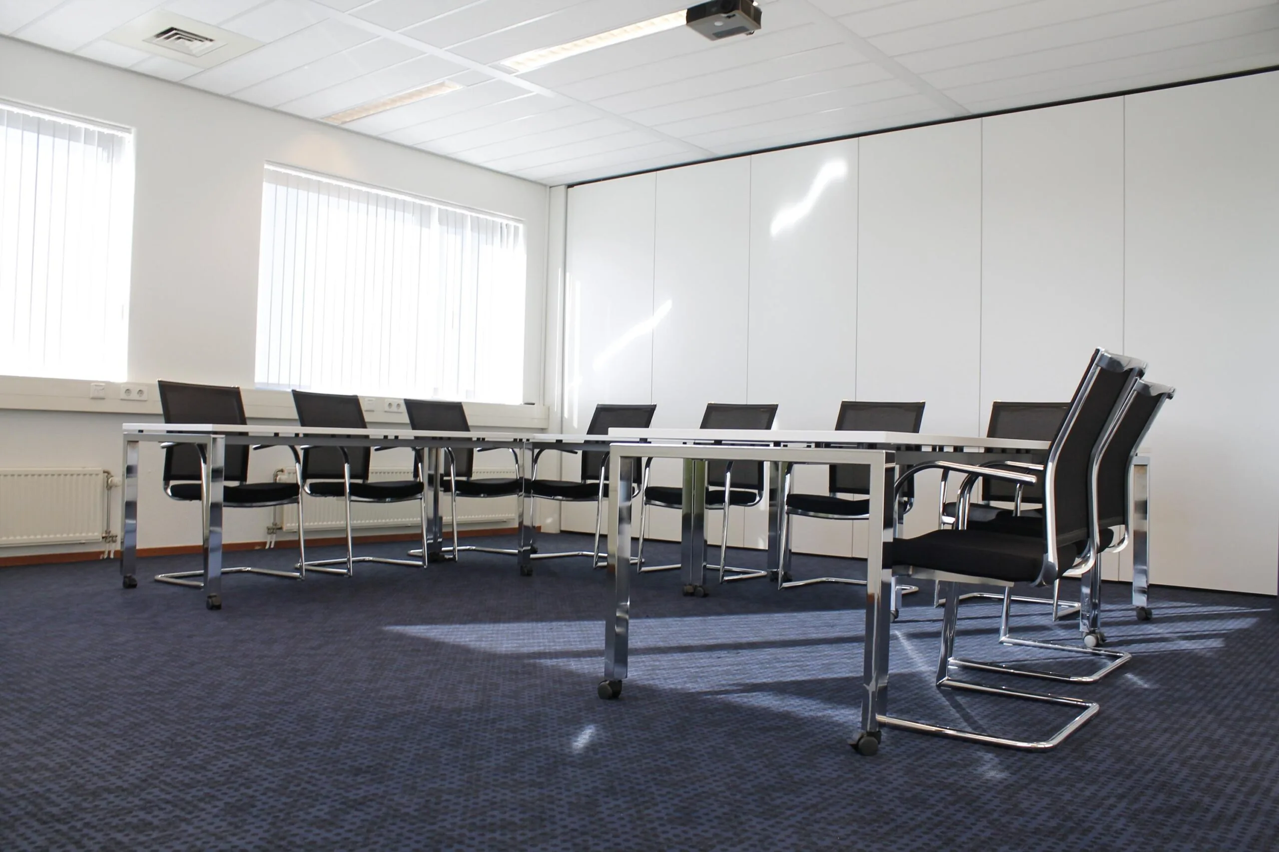 Vergaderruimte aan de Laan van ’s-Gravenmade met moderne stoelen, tafels en witte wandpanelen.