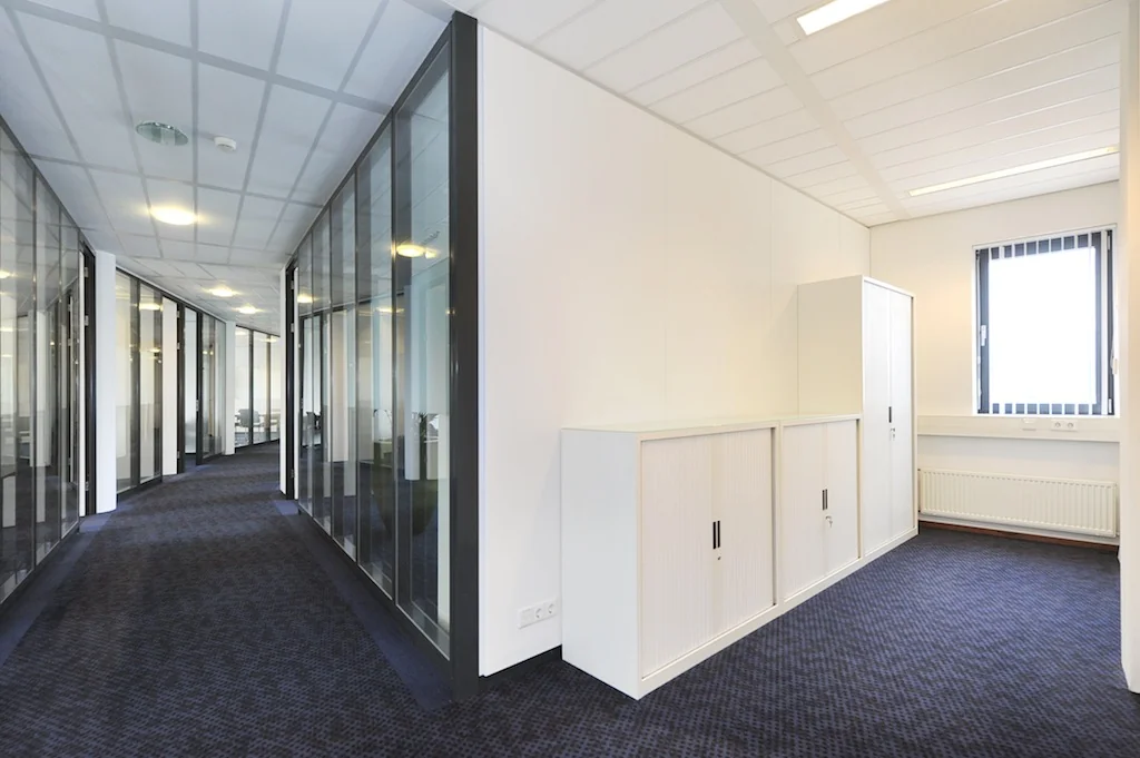 Moderne kantoorruimte aan de Laan van S-Gravenmade met glazen wanden, witte kasten en donkerblauw tapijt.