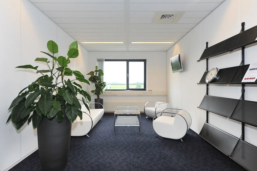 Wachtruimte met moderne witte stoelen, glazen tafels, grote planten en een wandrek in een kantoor aan de Laan van ’s-Gravenmade.