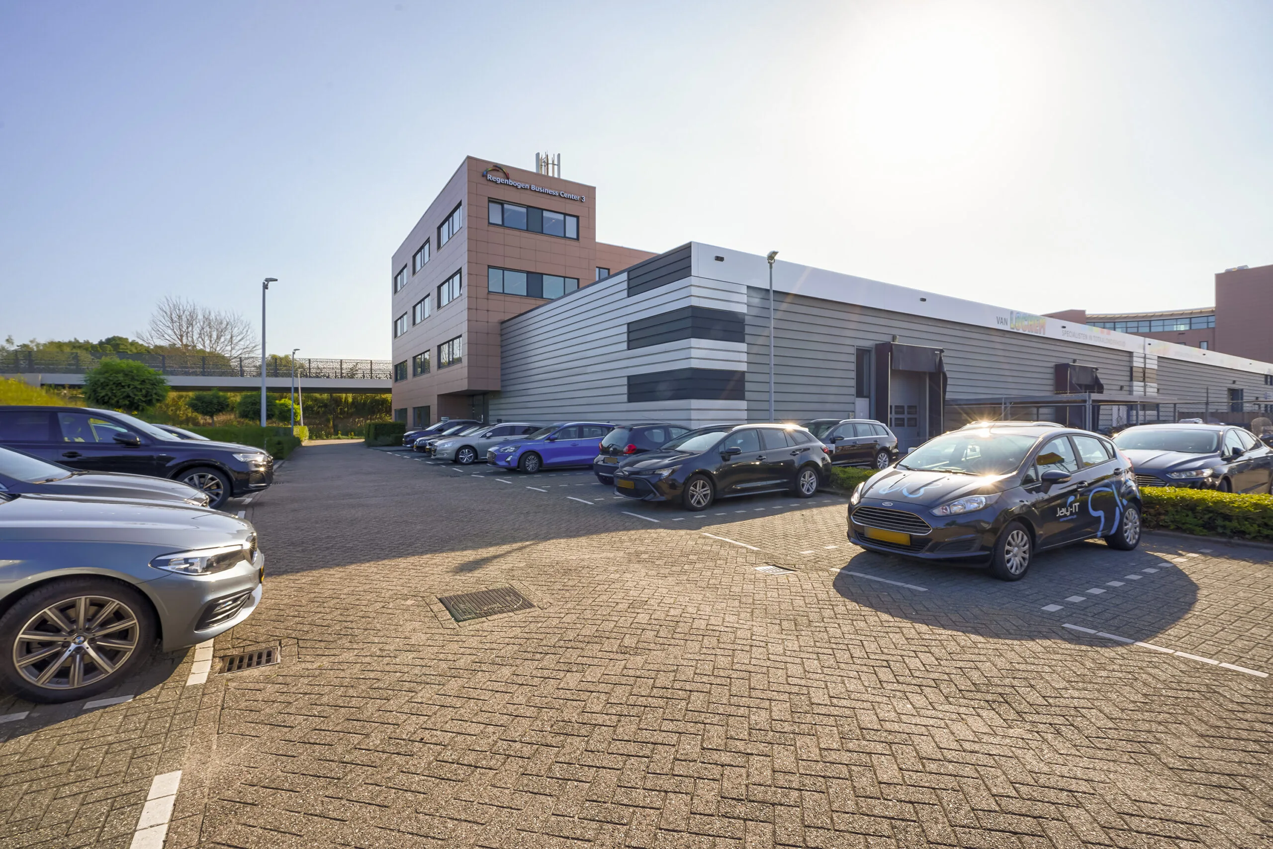 Parkeerterrein met geparkeerde auto’s voor het Regenbogen Business Center aan de Laan van ‘s-Gravenmade.