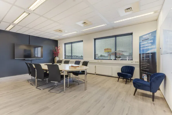 Moderne vergaderruimte aan de Laan van S-Gravenmade met een ovale tafel, negen stoelen, een groot presentatiescherm en natuurlijk licht door grote ramen.