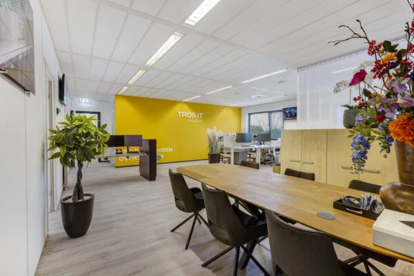 Modern kantoorinterieur van TROS IT Solutions aan de Laan van S‑Gravenmade met vergadertafel, werkplekken en gele accentmuur.
