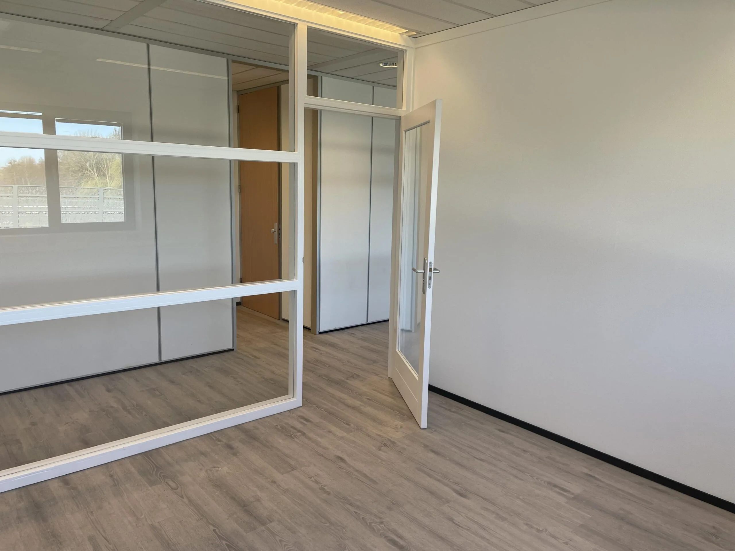 Leeg en modern kantoor met glazen binnenwanden en een open deur aan de Laan van ‘s-Gravenmade.