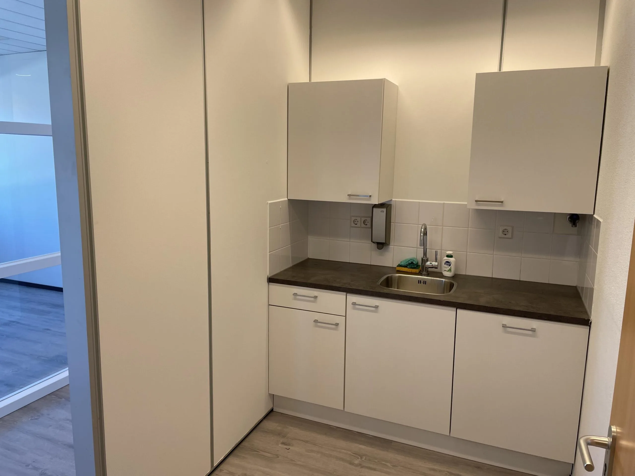 Kleine pantry met witte kasten, een spoelbak en schoonmaakspullen aan de Laan van S-Gravenmade.
