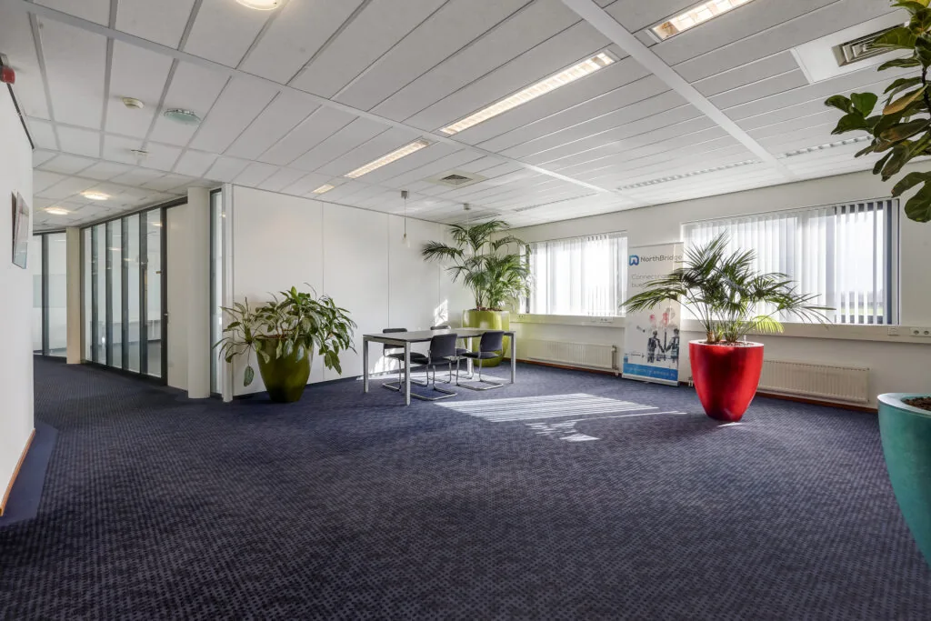 Moderne kantoorruimte aan de Laan van 's-Gravenmade met vergadertafel, grote plantenbakken en veel daglicht.