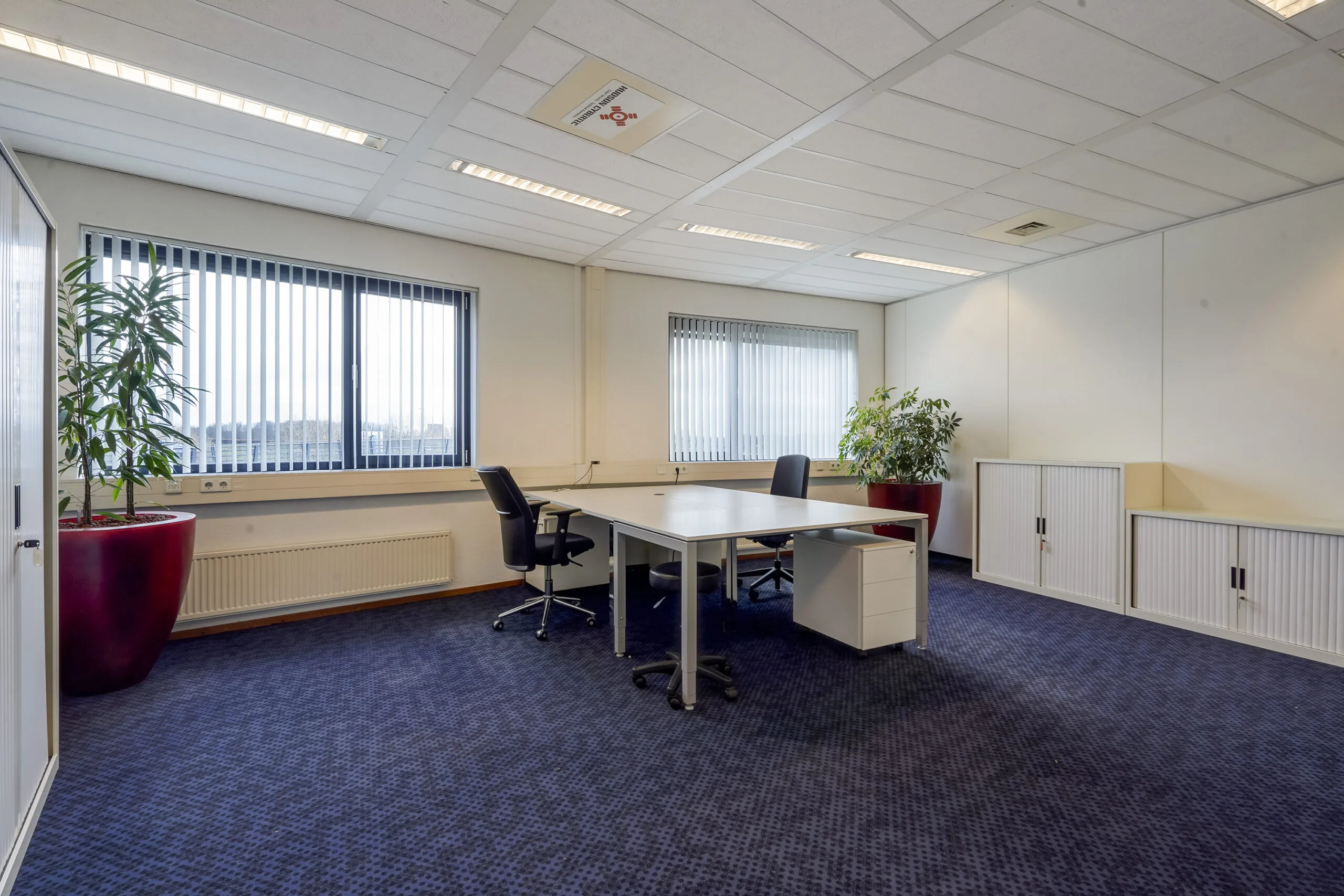Modern ingericht kantoor aan de Laan van S‑Gravenmade met twee bureaustoelen, grote ramen en planten in rode potten.