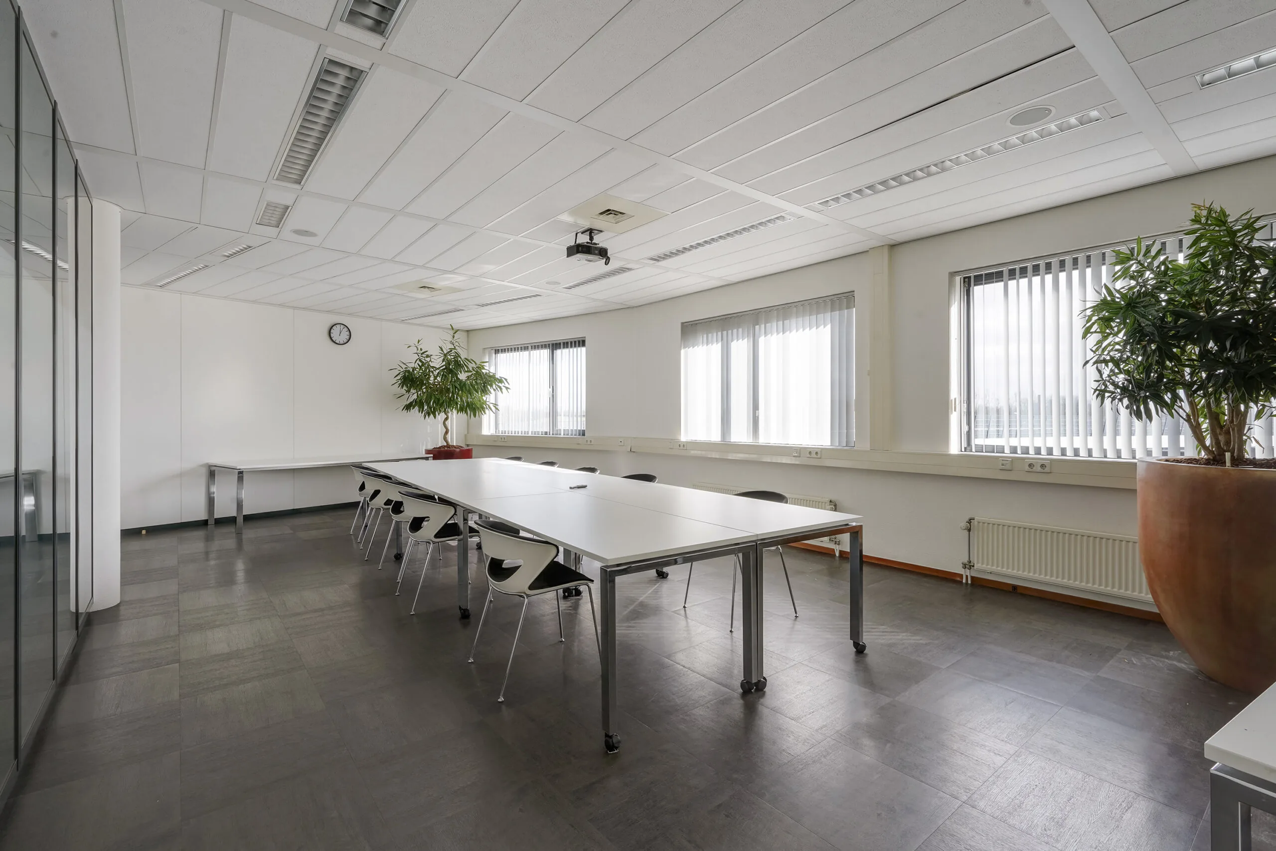 Vergaderruimte aan de Laan van S-Gravenmade met lange witte tafel, zwarte stoelen, grote planten en veel daglicht.