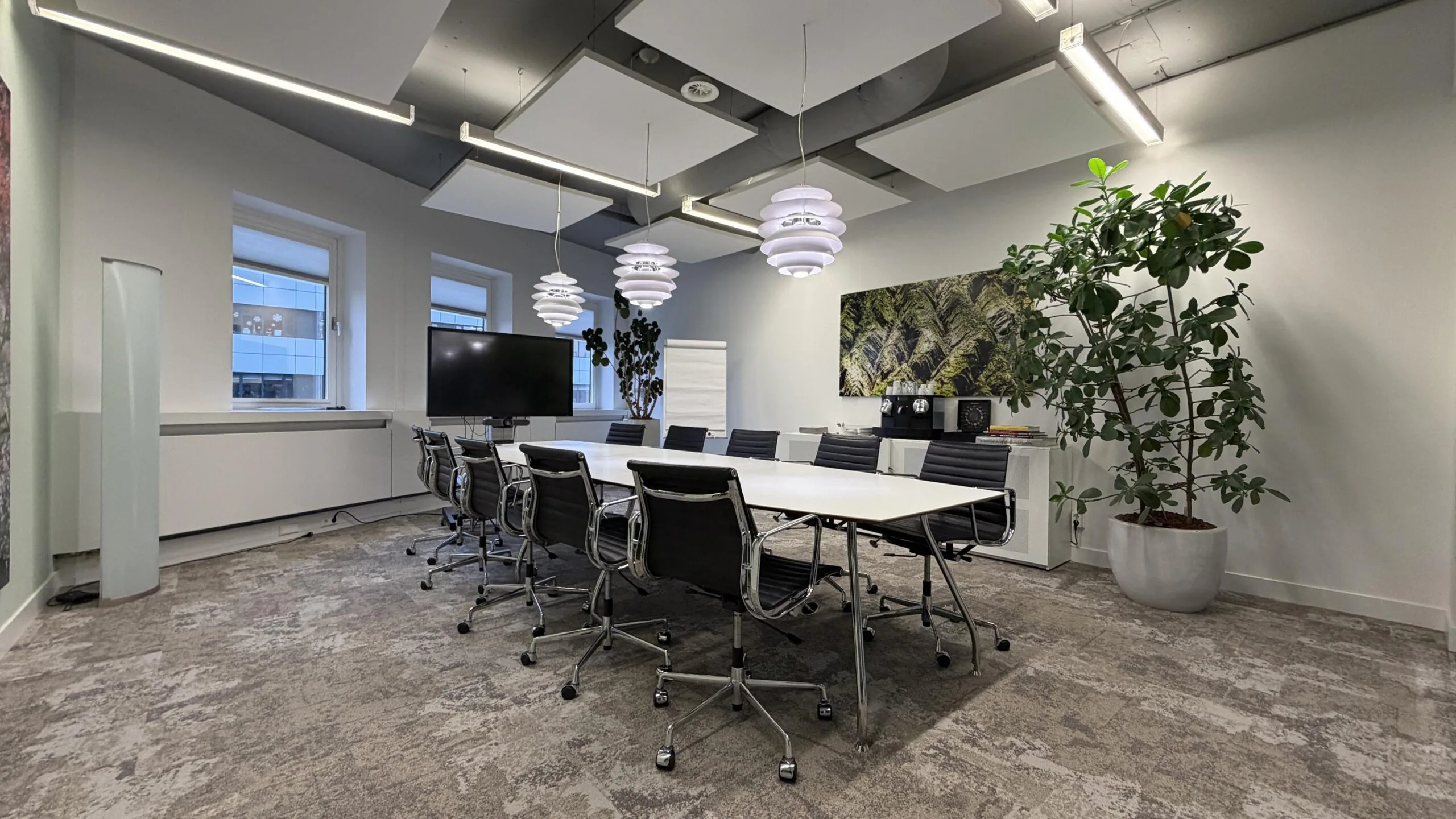 Moderne vergaderruimte aan de Euclideslaan met lange tafel, designstoelen, grote planten en een flatscreen.